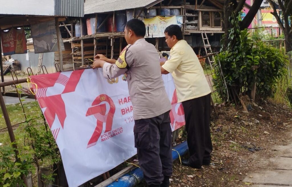 Bhabinkamtibmas Pasang Spanduk HUT Bhayangkara ke-79 Bersama Petugas Keamanan.