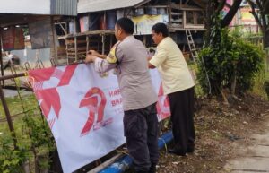 Bhabinkamtibmas Pasang Spanduk HUT Bhayangkara ke-79 Bersama Petugas Keamanan.